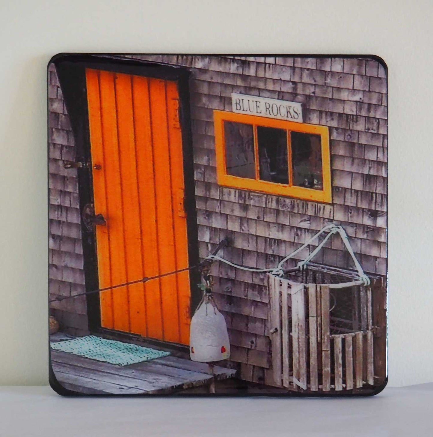 Unique and charming spot in Nova Scotia. Blue Rocks, a cozy little harbor with lots of little fishing shacks. It's still a working fishing village, with blue slate rocks at the ocean's edge. Blue Rocks shingles house with a orange door that you can miss. Resin-coated 8 x 8 inches photography. Ready to hang