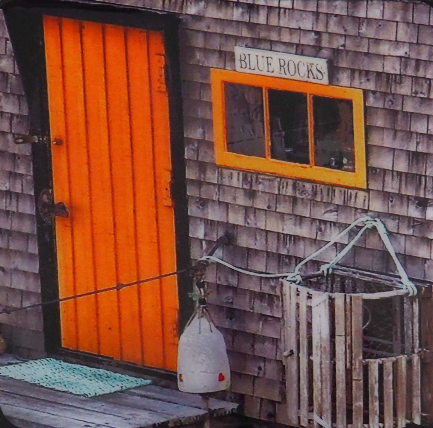 Unique and charming spot in Nova Scotia. Blue Rocks, a cozy little harbor with lots of little fishing shacks. It's still a working fishing village, with blue slate rocks at the ocean's edge. Blue Rocks shingles house with a orange door that you can miss. Resin-coated 8 x 8 inches photography. Ready to hang