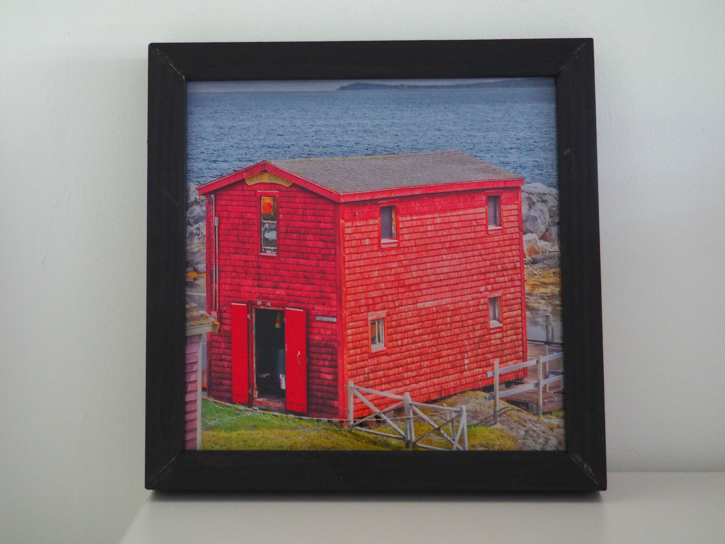Spectacular view of Blue Rocks harbour featuring a picturesque red barn.   Photography 7.5 x 7.5 inches covered with resin in a handmade black wooden frame 9 x 9 inches.  Ready-to-hang in your favorite room.